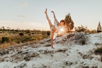 a woman is doing yoga on a rock at sunset