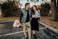 a man and woman standing in a parking lot with a guitar